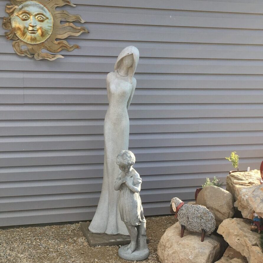 A statue of a woman and child in front of a wall.